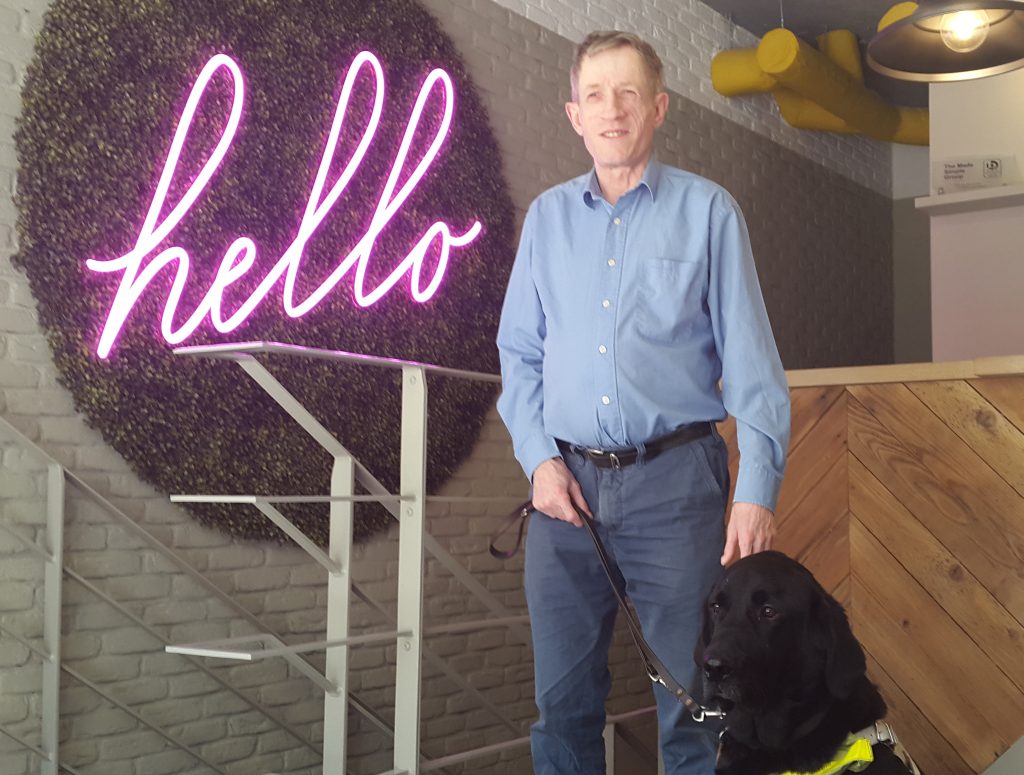 smartly dressed visually impaired man with guide dog standing by our office reception desk